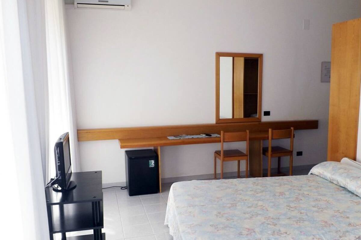 Une chambre d’hôtel comprenant un lit, un bureau avec une chaise, un miroir et un téléviseur.