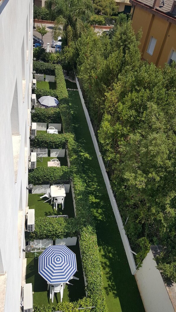 Vista aérea de um pátio com um caminho estreito, rodeado por vegetação exuberante e edifícios brancos.