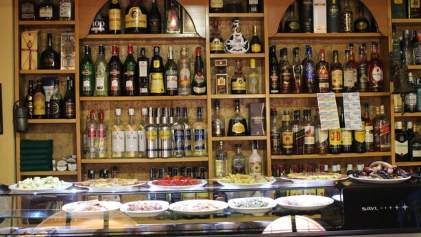 Een bar met flessen drank achter een schap en een vitrine met etenswaren.