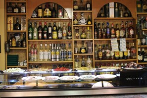 Een bar met flessen drank achter een schap en een vitrine met etenswaren.