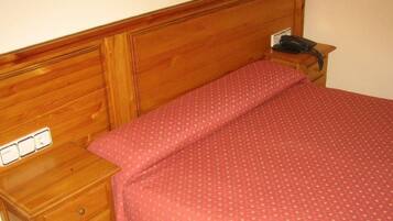 Una cama de madera con colcha de lunares rojos y una mesita de noche de madera con un teléfono.