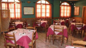 Un comedor con varias mesas cubiertas de manteles rojos, sillas de madera y amplias ventanas con cortinas.