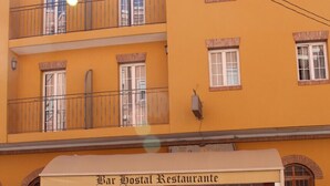 Een geel gebouw met balkon en een restaurant genaamd "Bar Hostal Restaurante" aan de voorzijde.