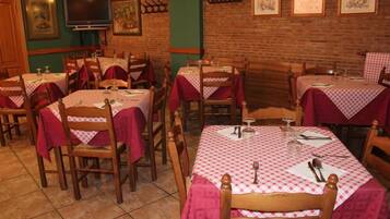 A restaurant with multiple tables covered with red and white checkered tablecloths, wooden chairs, and a brick wall backdrop.