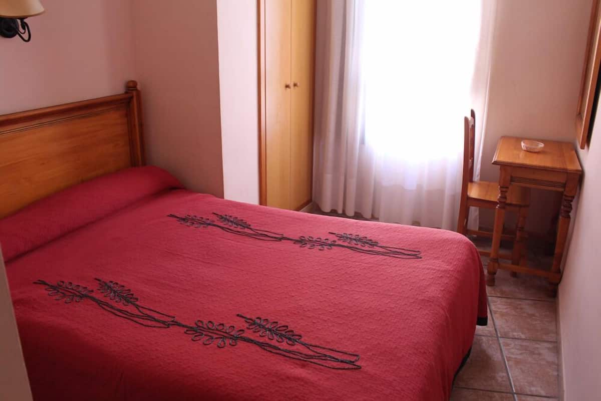 Une chambre à coucher avec un lit en bois, une table de chevet en bois, une chaise et une petite table sur laquelle se trouve un bol.