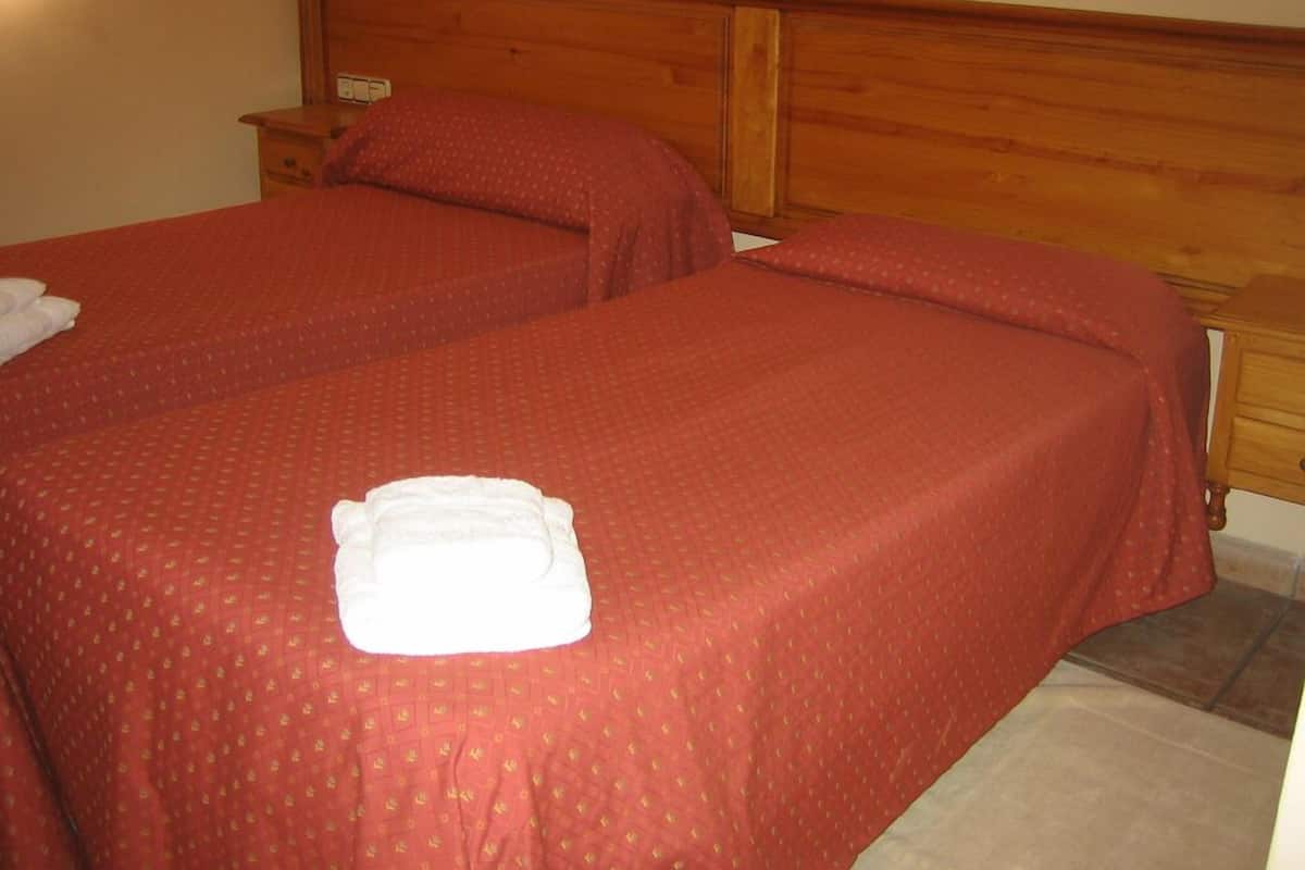 Une chambre d’hôtel avec deux lits simples, chacun recouvert d’une courtepointe rouge et doté d’oreillers, d’une tête de lit en bois et d’une table de chevet avec une lampe.