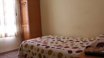 Un dormitorio con una cama cubierta por una colcha estampada, un armario de madera y una mesita de noche con un control remoto.