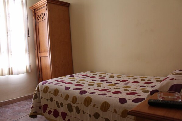 Une chambre à coucher avec un lit recouvert d’une couvre-lit à motifs, une armoire en bois et une table de chevet avec une télécommande.