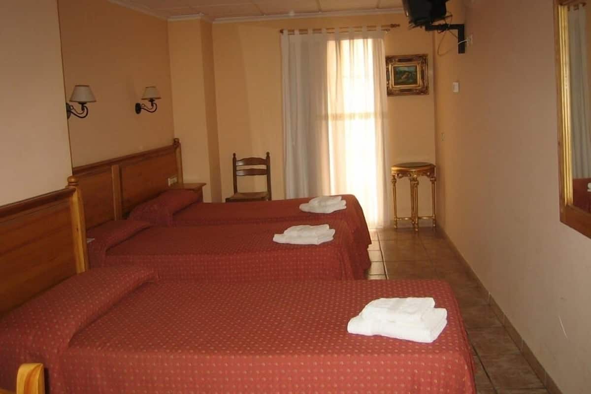 Une chambre d’hôtel avec deux lits, une chaise, une petite table et un tableau au mur.