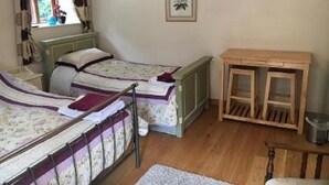 A room with two single beds, a wooden table, and a window with curtains. - The Lampet Arms (Banbury)