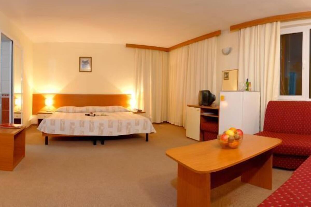 A hotel room with a bed, a red sofa, a small table, and a window with curtains.