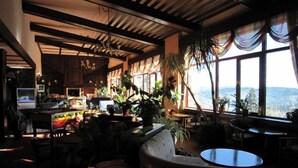 Un restaurante acogedor y bien iluminado, con vigas de madera, grandes ventanales que ofrecen vistas a las montañas y diferentes disposiciones de asientos, incluidas mesas y sillas.