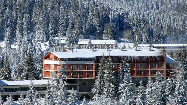 Una cabaña de varios pisos con fachada roja, rodeada de árboles cubiertos de nieve.