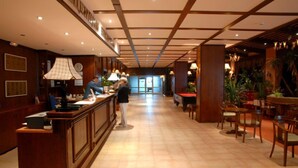 Un vestíbulo de hotel con una recepción, un área de espera con sillas y un comedor con mesas y sillas.