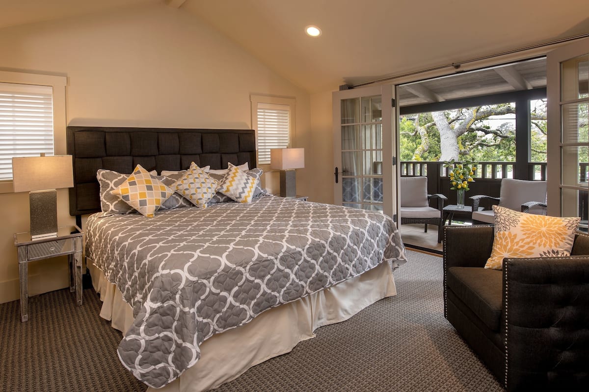 A bedroom with a large bed, two bedside tables, a nightstand, a sofa, and a view of the outdoors.