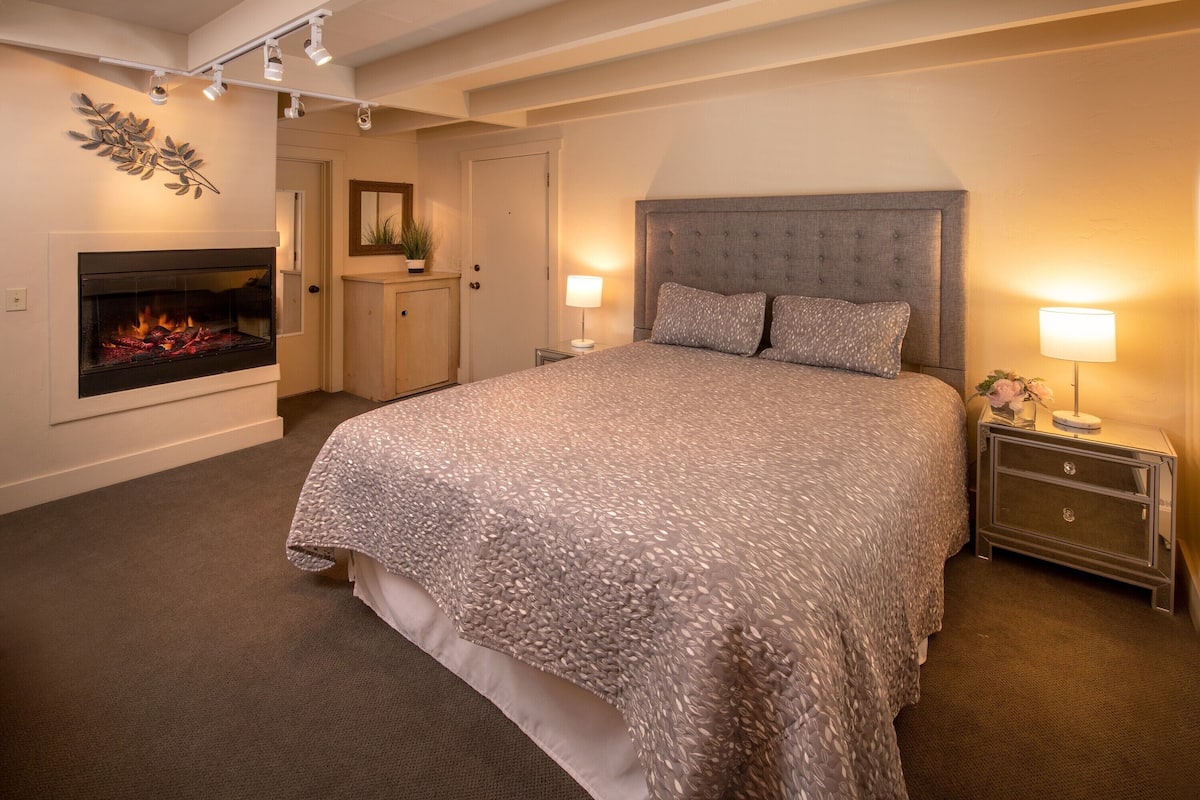 A bedroom with a large bed, a fireplace, and two bedside lamps.