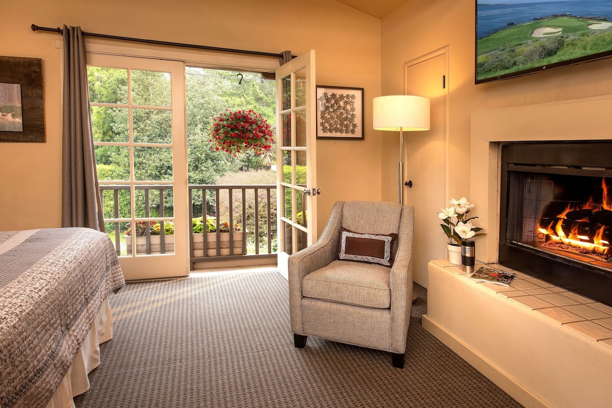 A hotel room with a bed, a chair, a fireplace, a TV, and a balcony with a hanging flower basket.