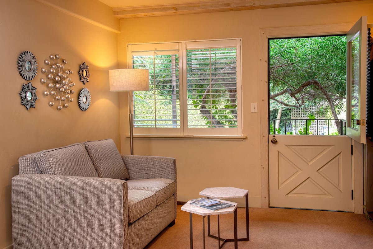 A living room with a sofa, a lamp, a table, and a door with a view of greenery.