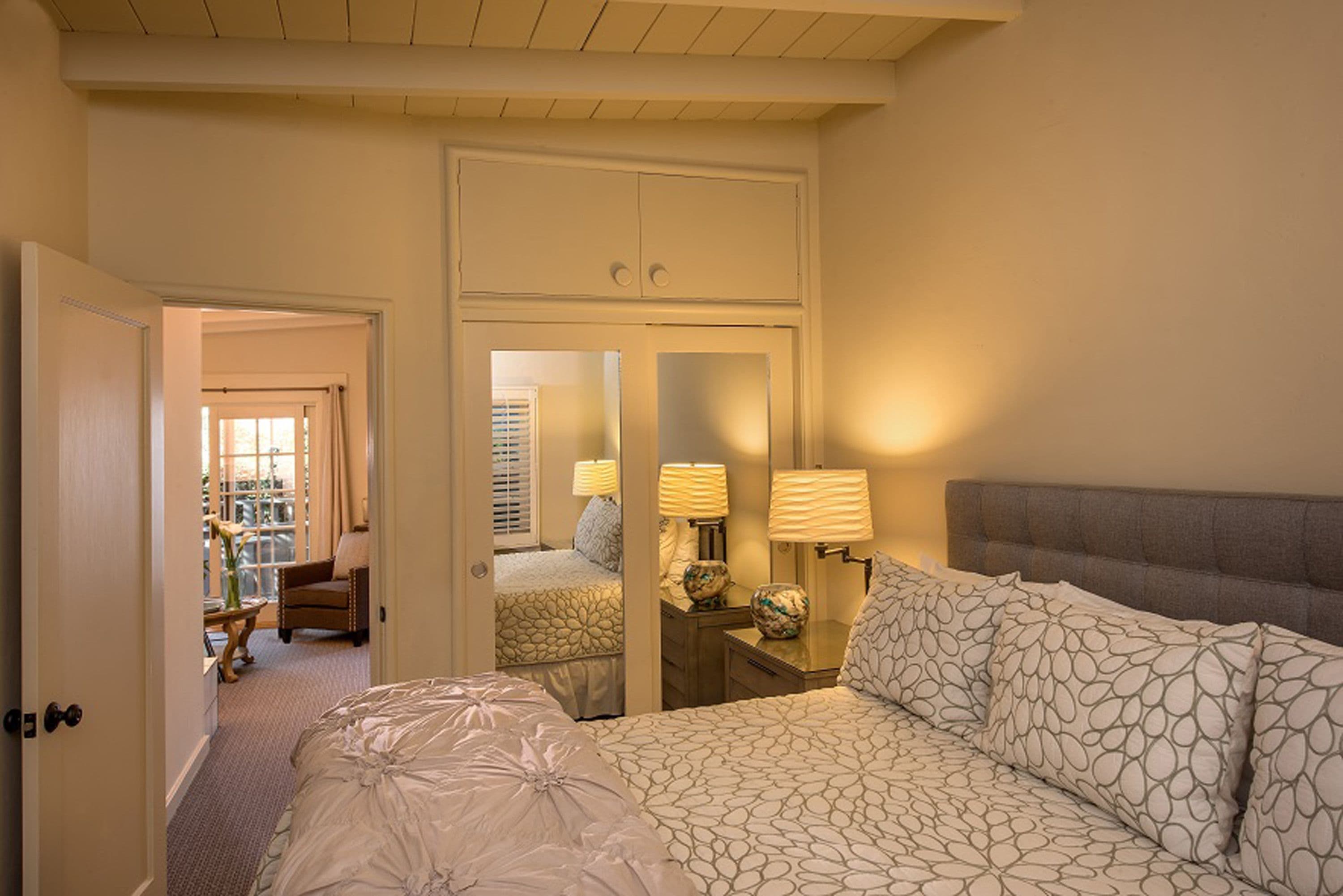 A hotel room with a large bed, a bedside table with lamps, a mirror, and a wardrobe.