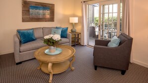 A living room with a grey sofa, a round wooden coffee table with a vase of flowers, a grey armchair, and a view of the outdoors through a glass door. - Carmel Country Inn (Carmel)
