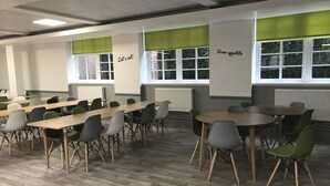 A classroom with tables and chairs, a projector screen, and a window with a view of trees. - Bowden Court - Hostel (London)
