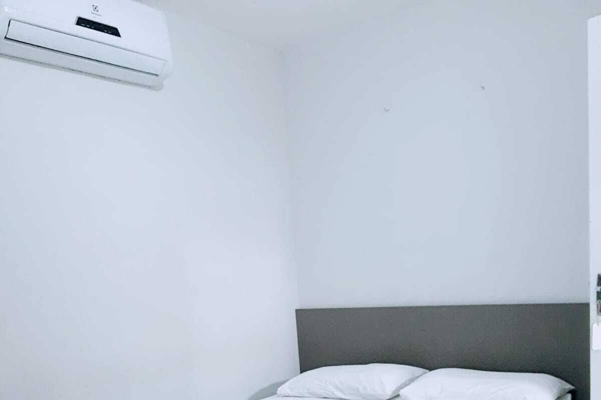 A small, clean room with a single bed, a bedside table, and a wall-mounted air conditioning unit.