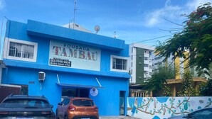 A blue building with a sign reading "POSADA TAMIBAU" and a parking area with two cars. - Pousada Tambaú (João Pessoa)