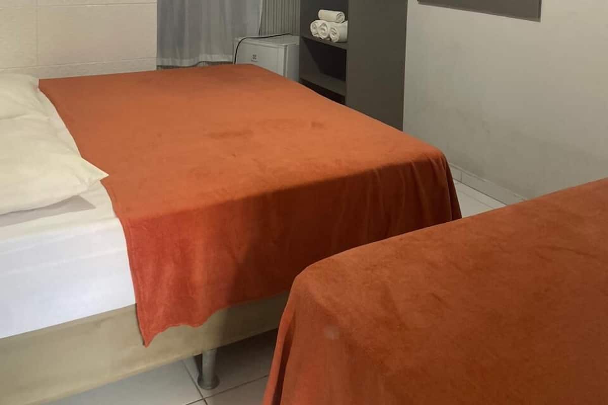 A small, clean room with two beds, a TV mounted on the wall, and a shower area.