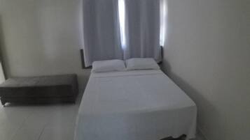A single-bed room with a headboard, a bedside table, and a window with curtains.