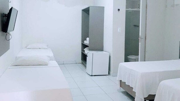 A hotel room with three single beds, a small white refrigerator, a TV mounted on the wall, and a walk-in closet. - Pousada Tambaú (João Pessoa)