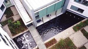 Ein Luftbild eines modernen Gebäudes mit einem zentralen Innenhof, einem Wasserspiel und umliegender Bepflanzung.