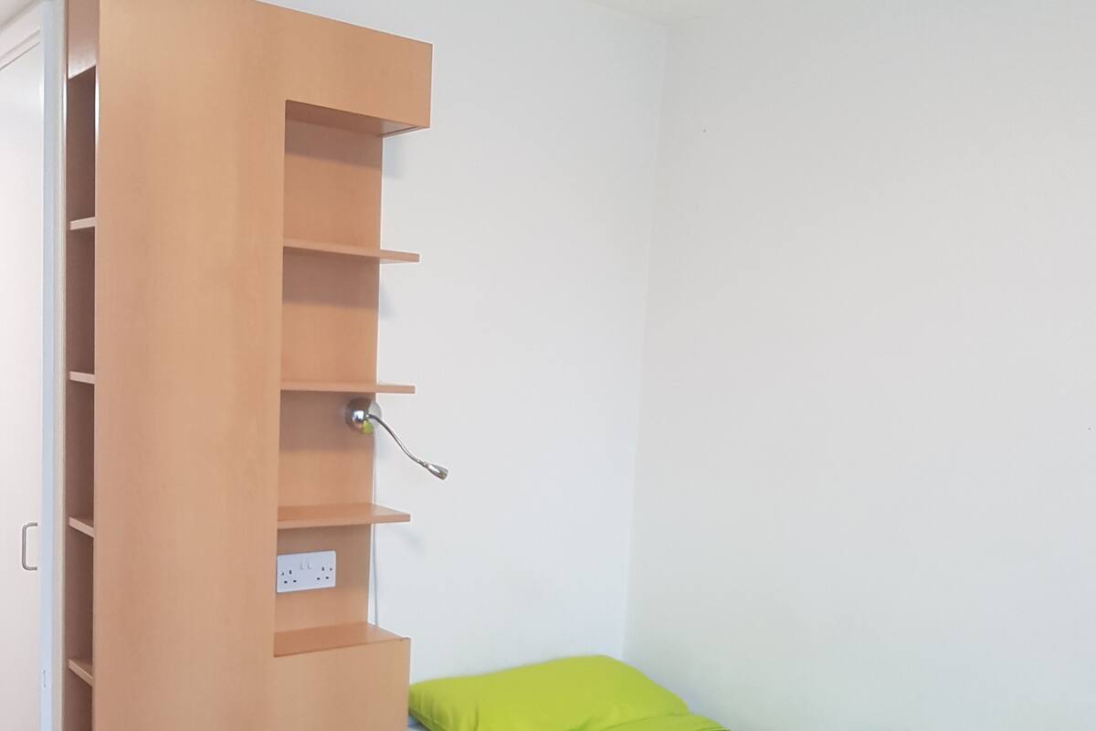 Une petite chambre avec un lit simple, une armoire en bois et une couvre-lit verte.