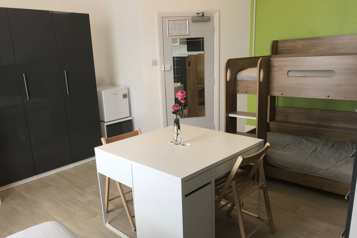 A compact room with a kitchenette, a small dining table, a bed, and a large wardrobe.