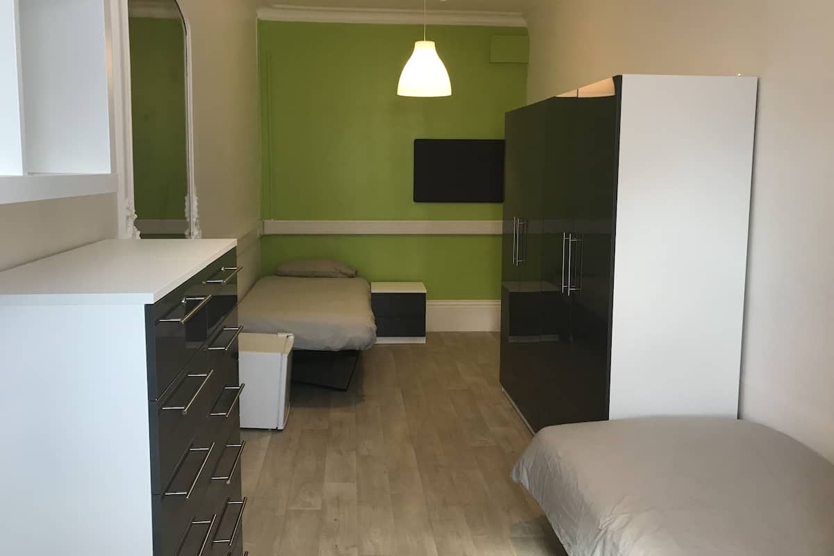 A compact room with a bed, a small desk, a wardrobe, and a TV mounted on the wall.