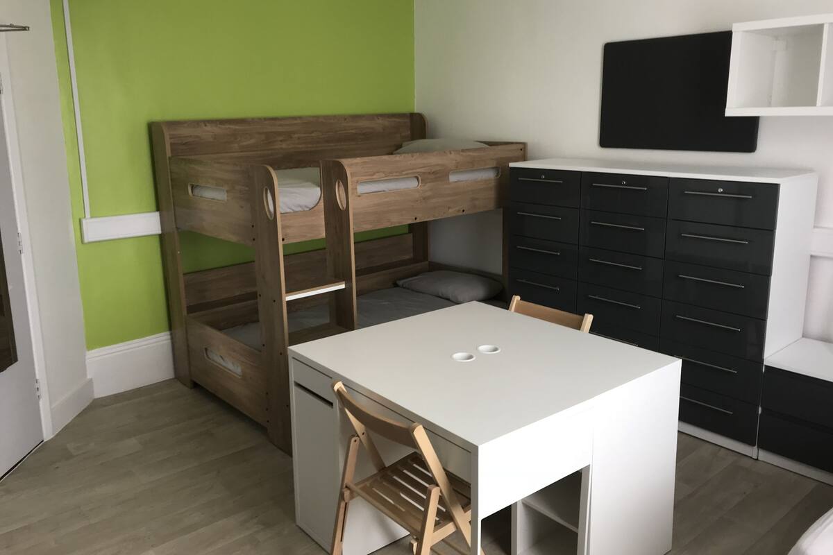 A room with bunk beds, a desk, a chair, and a wardrobe.