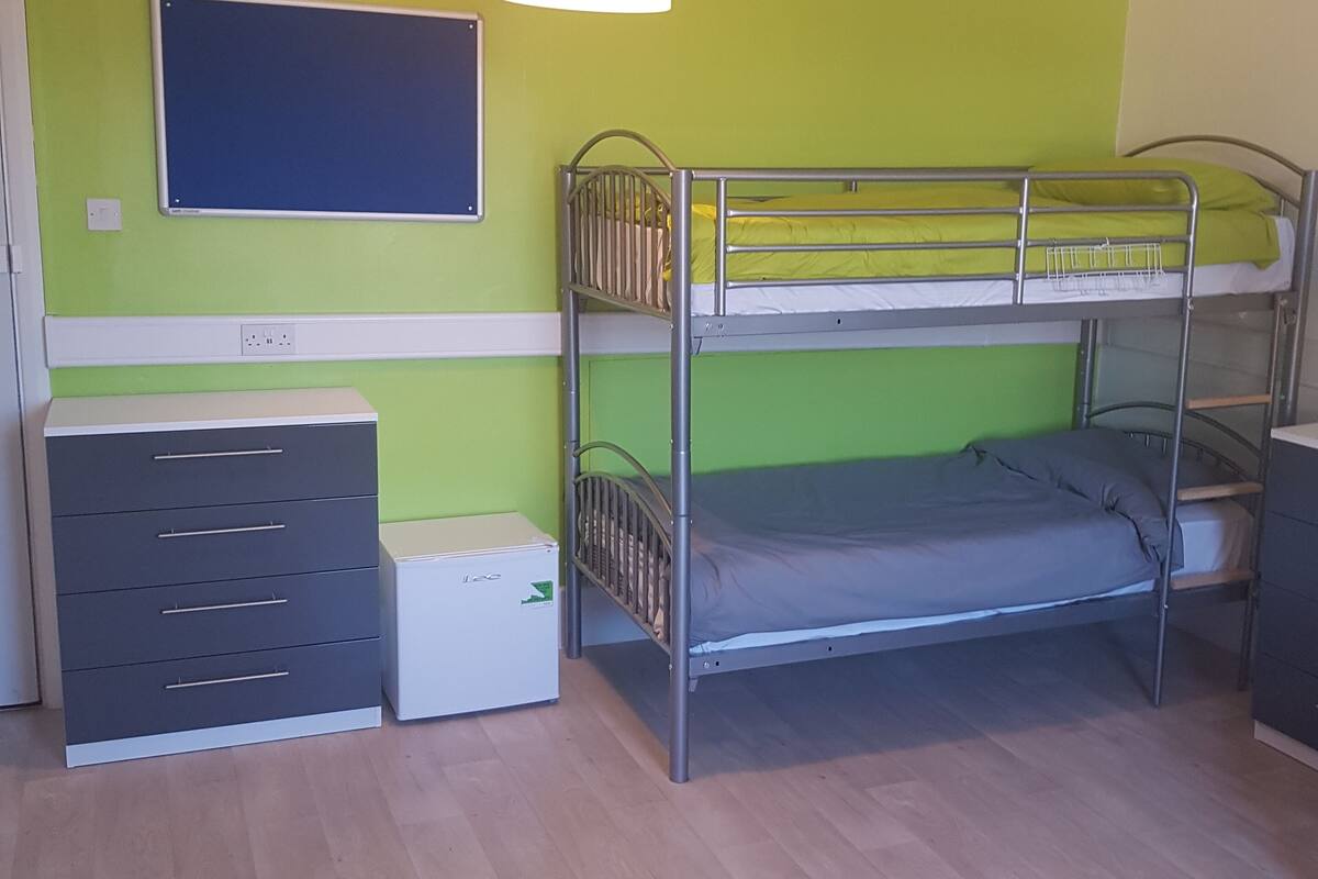 A bunk bed room with a desk and drawers, a whiteboard, and a ceiling light.