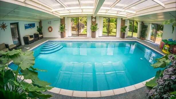 A large indoor swimming pool with a glass ceiling, surrounded by potted plants and a seating area. - Sea View Holiday Flat - Covehurst Bay (Hastings)