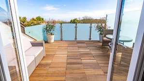 A balcony with a wooden floor, wicker furniture, and potted plants. - Sea View Holiday Flat - Covehurst Bay (Hastings)