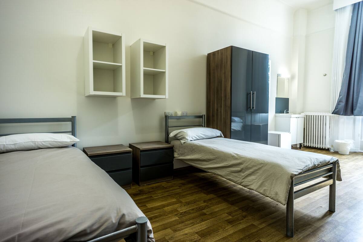 A modern bedroom with two single beds, a wardrobe, a bedside table, and a radiator.
