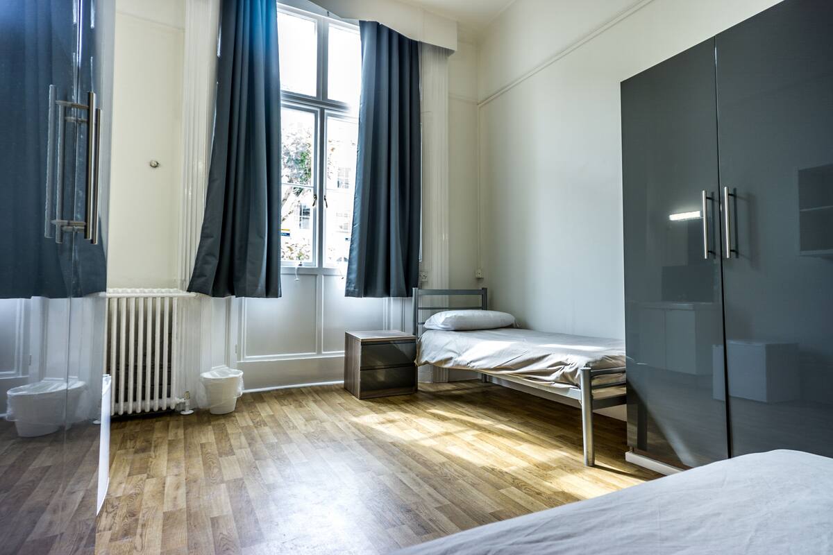 A bedroom with a bed, a wardrobe, a radiator, and a window with curtains.