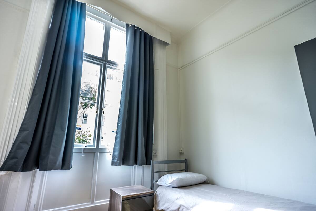 A small, neatly arranged bedroom with a single bed, a nightstand, and a window with curtains.