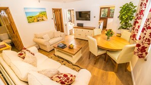A living room with a sofa, coffee table, TV, dining table, chairs, and a potted plant. - Covehurst Bay Holiday Cottages (Hastings)