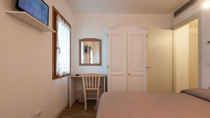 A bedroom with a bed, a desk, a chair, a wardrobe, and a television on a shelf.