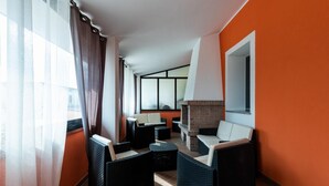 A modern lounge area with wicker furniture, a brick fireplace, and large windows with curtains.