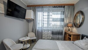 A hotel room with a bed, two chairs, a small table, a TV, a lamp, and a mirror. - Villa Asesor (Gdansk)
