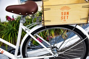 A white bicycle with a brown leather seat and a wooden box attached to the rear, labeled "SUNSET INN."
