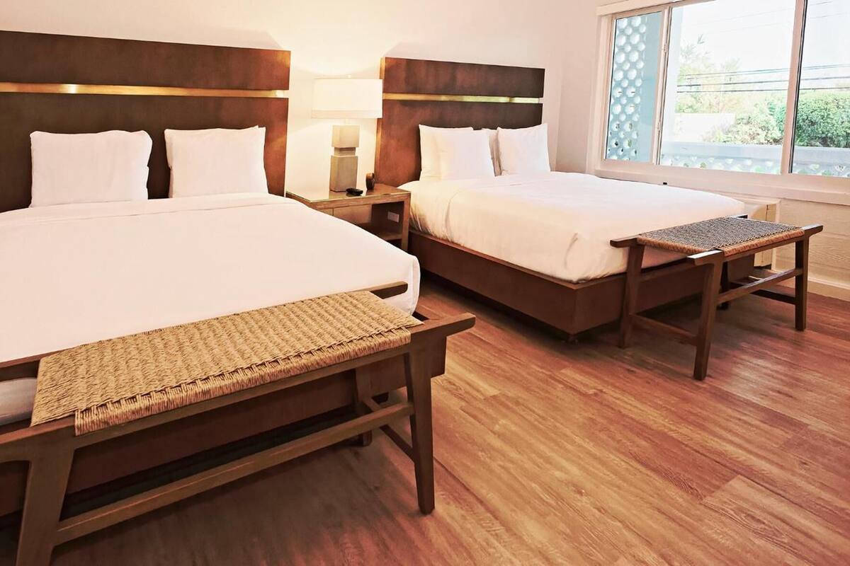 A hotel room with two beds, a small table, and a window with a view.