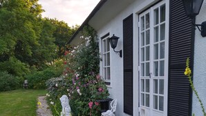 Une maison avec un chemin de pierre menant à l’entrée, entourée d’une végétation luxuriante et de plantes en fleurs.
