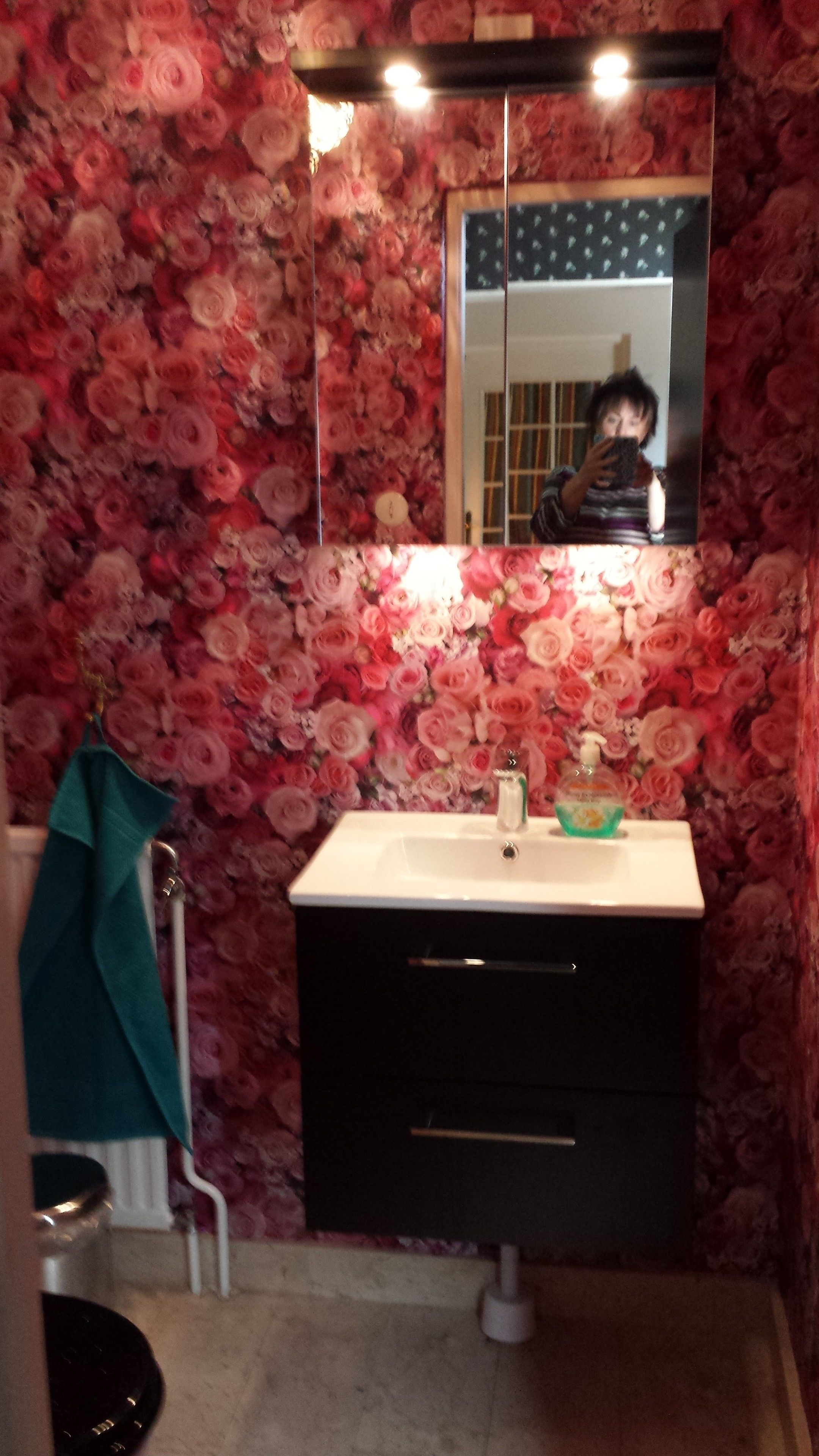 A bathroom with a floral wallpaper, a sink with a mirror above it, and a towel hanging on a rack.