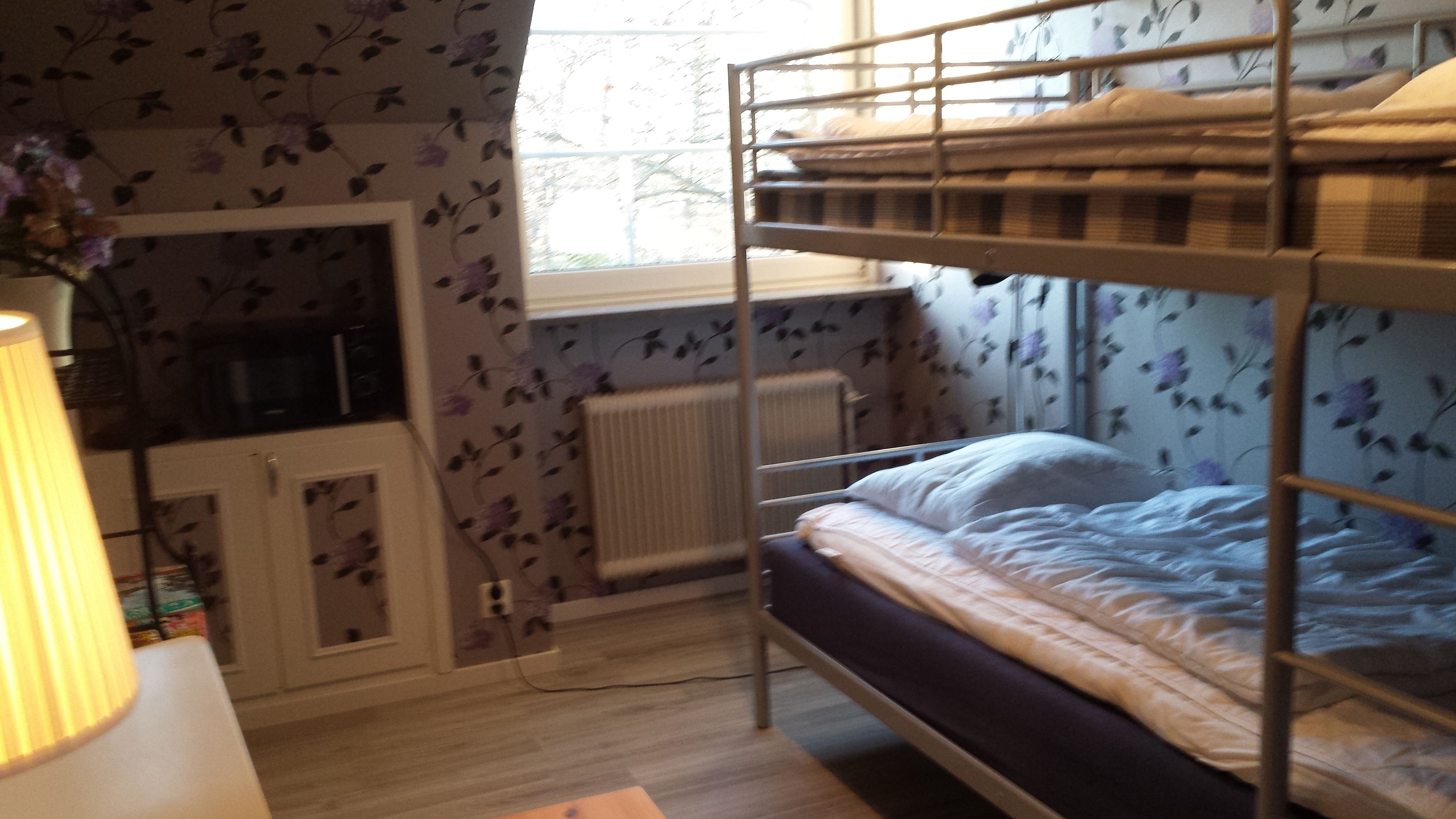 A bunk bed room with a radiator, a desk, and a window with floral wallpaper.